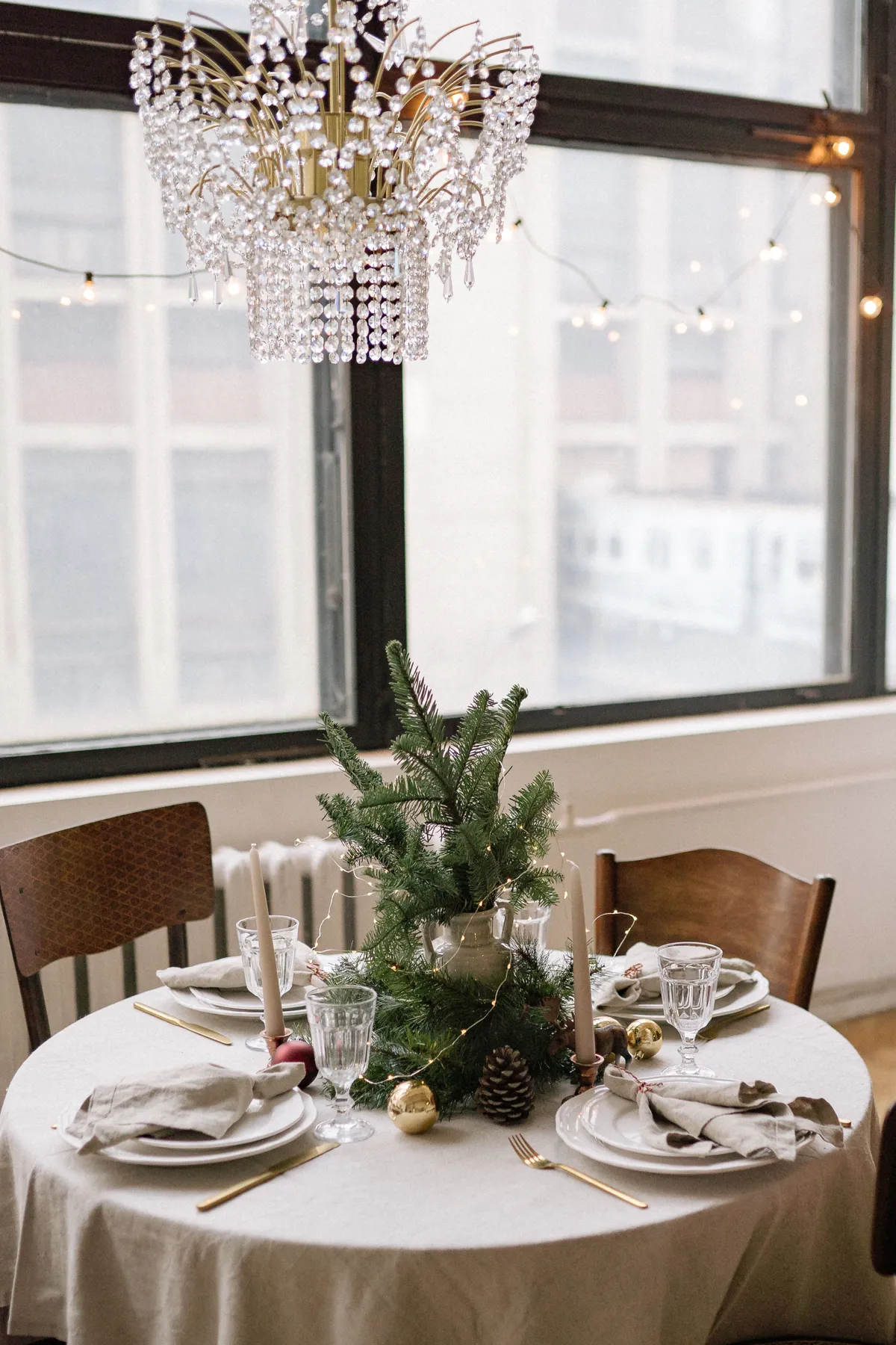 A beautifully decorated round table set for Christmas with a chandelier and festive decor.