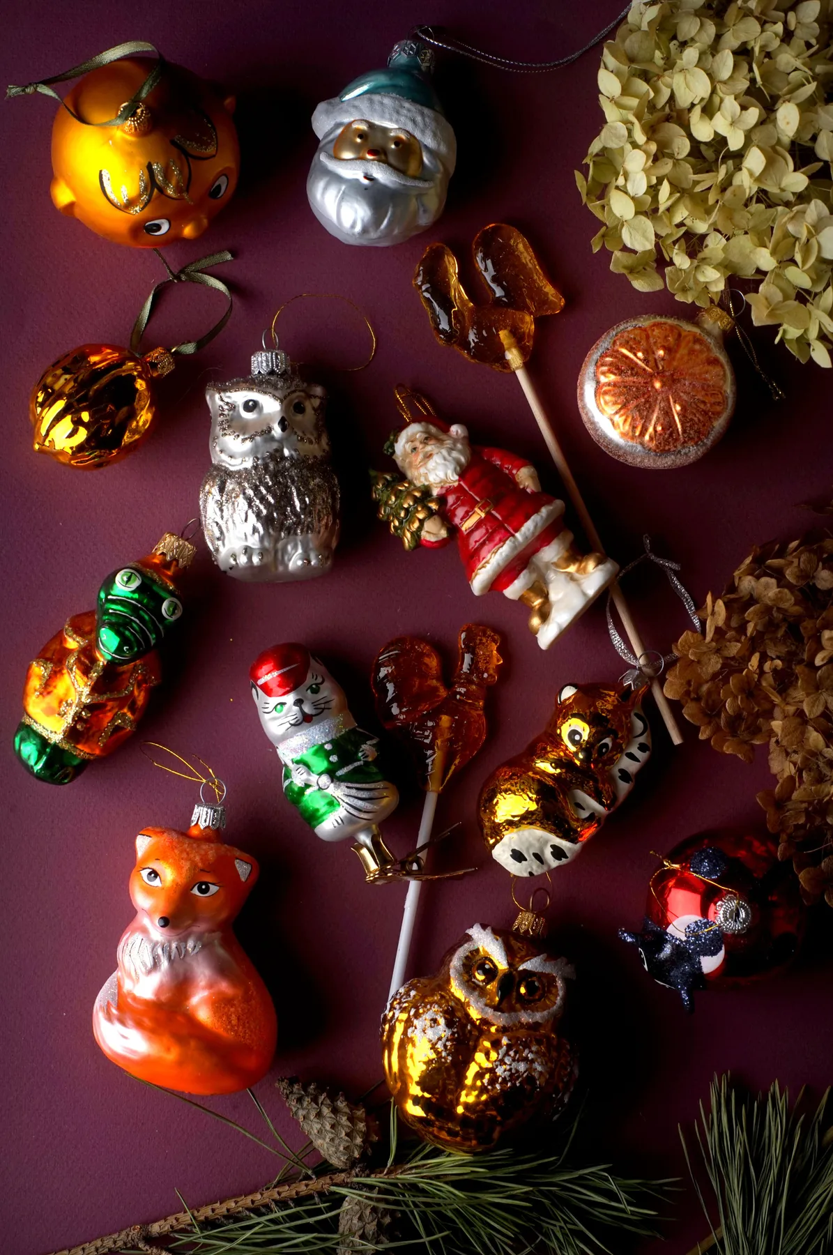 A charming flat lay of assorted vintage Christmas ornaments on a burgundy background.