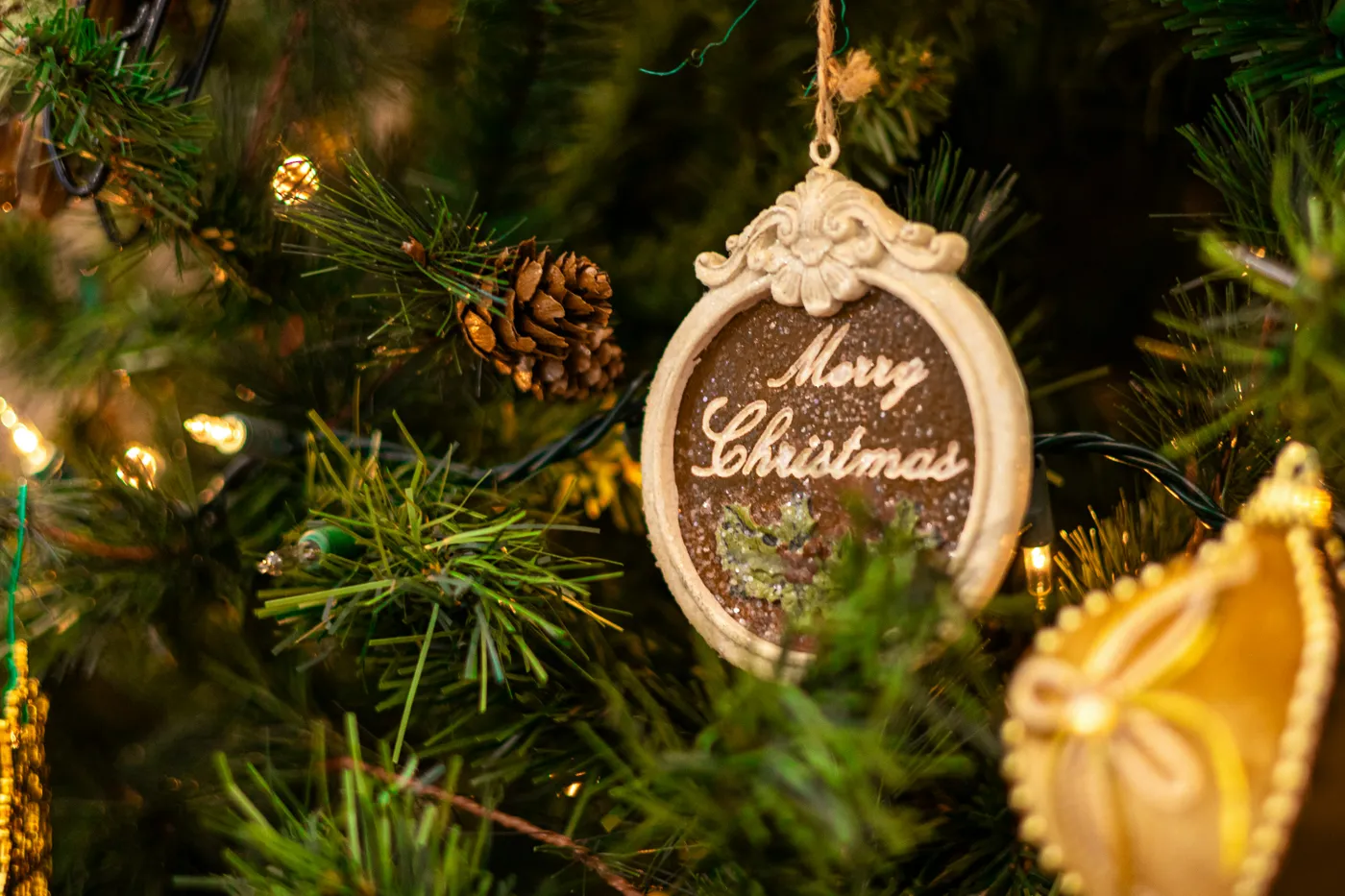 A close up image of an ornament reading “Merry Christmas” in cursive font on a Christmas tree.