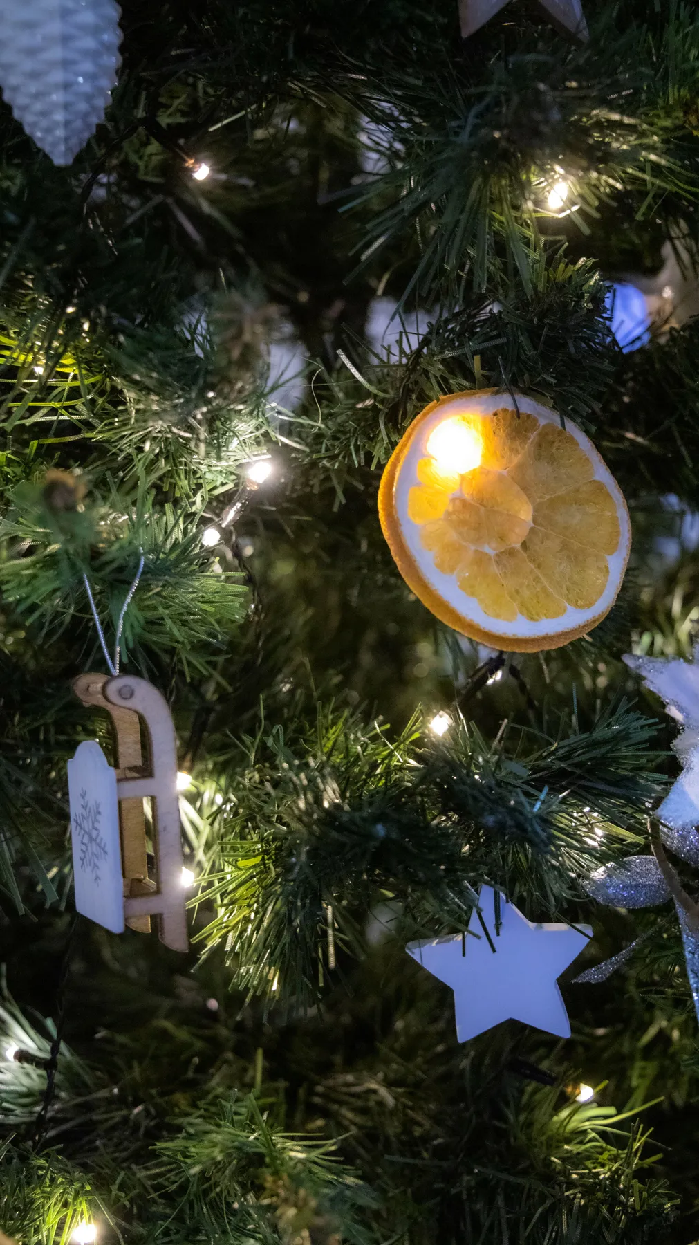A close-up of a festive Christmas tree decorated with ornaments, dried orange slice, and string lights.