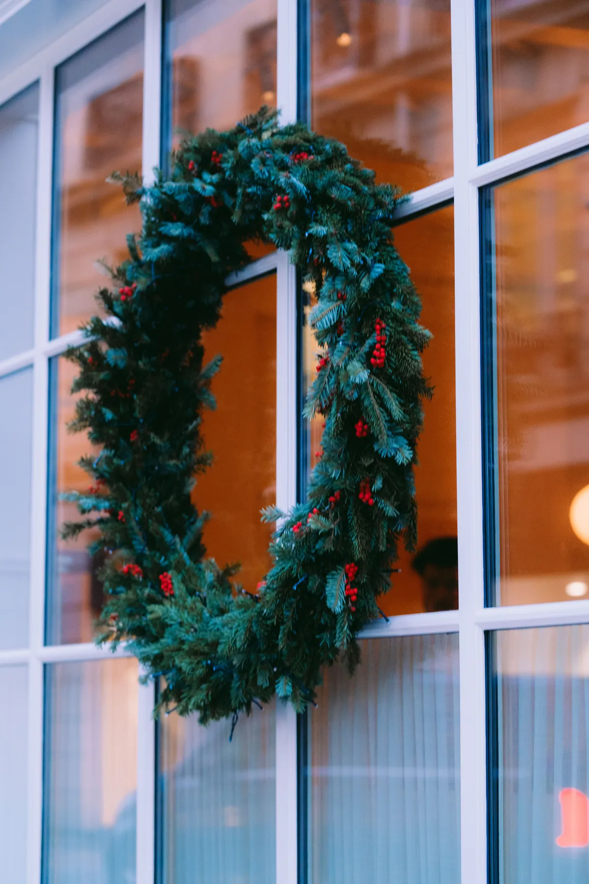 A decorative Christmas wreath with red berries hangs on a window, evoking holiday spirit.