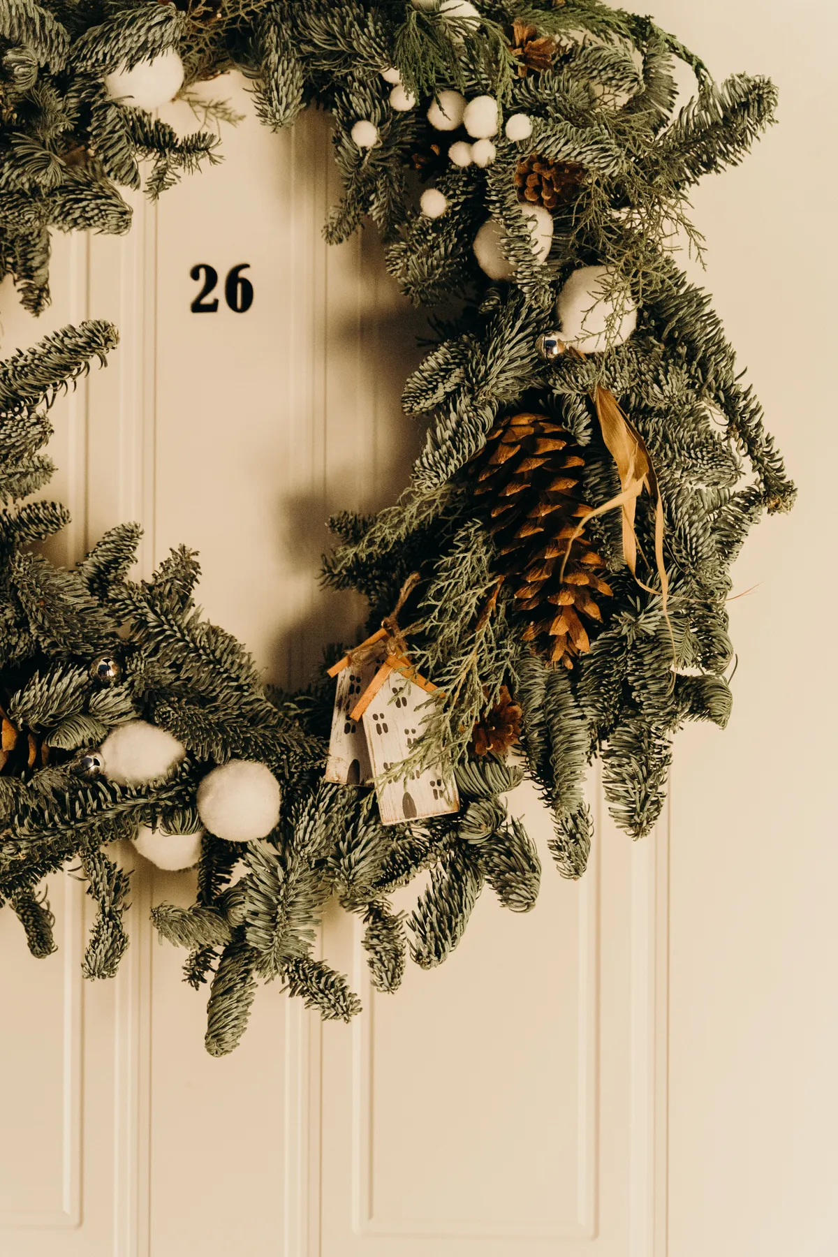 A festive Christmas wreath with pinecones and ornaments on a white door, perfect for holiday decor.