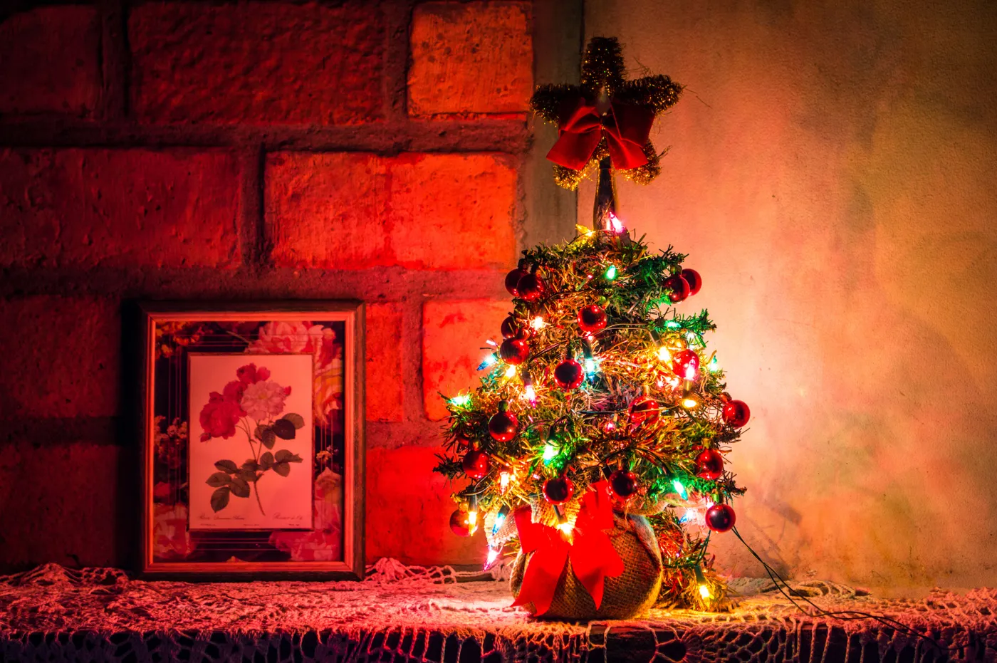 A small illuminated Christmas tree with colorful lights next to floral wall art.