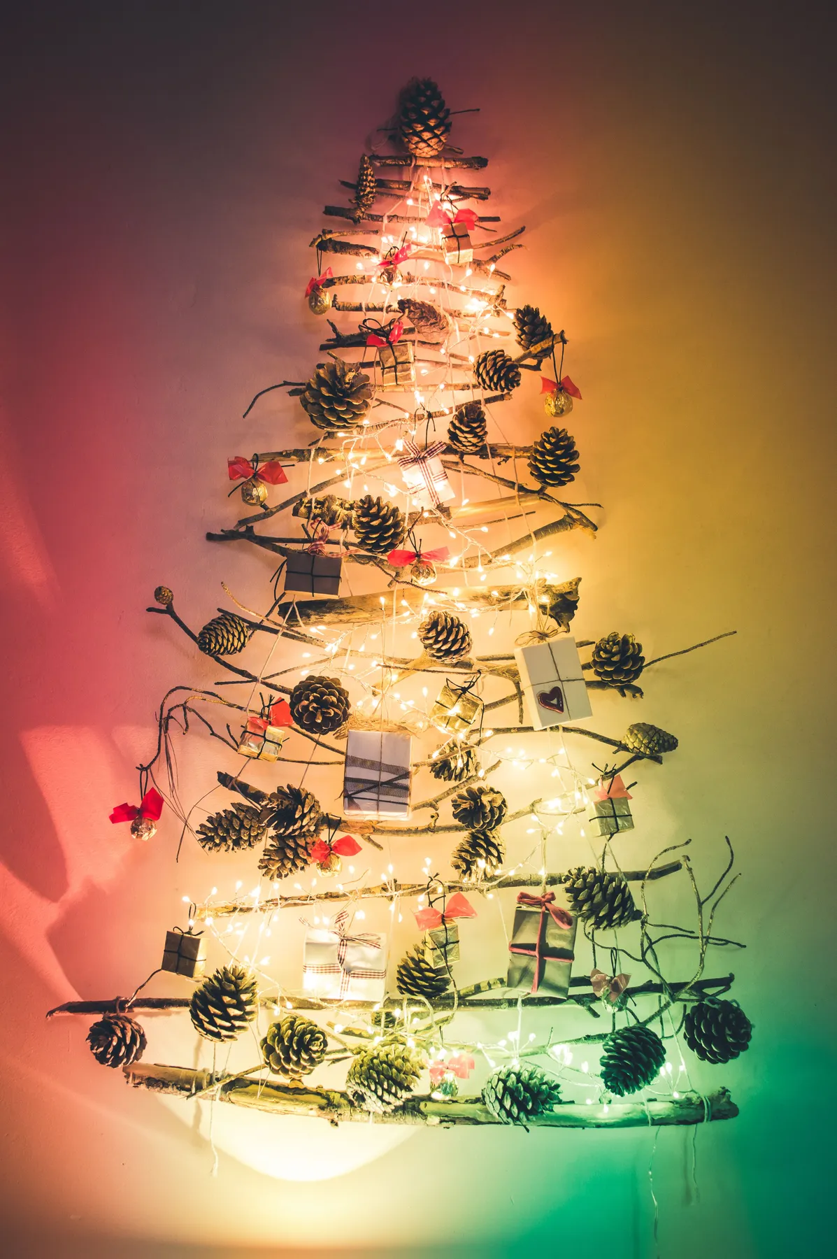 A unique wall-mounted Christmas tree decorated with pine cones, lights, and gift boxes.