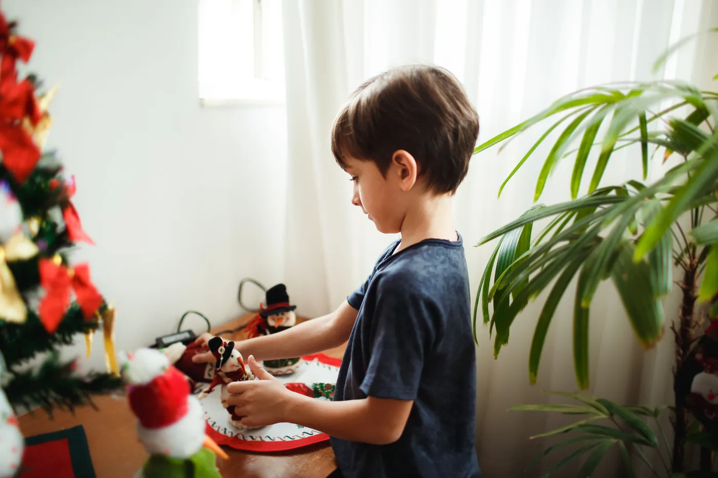 A young boy joyfully decorates a Christmas tree inside a cozy room.