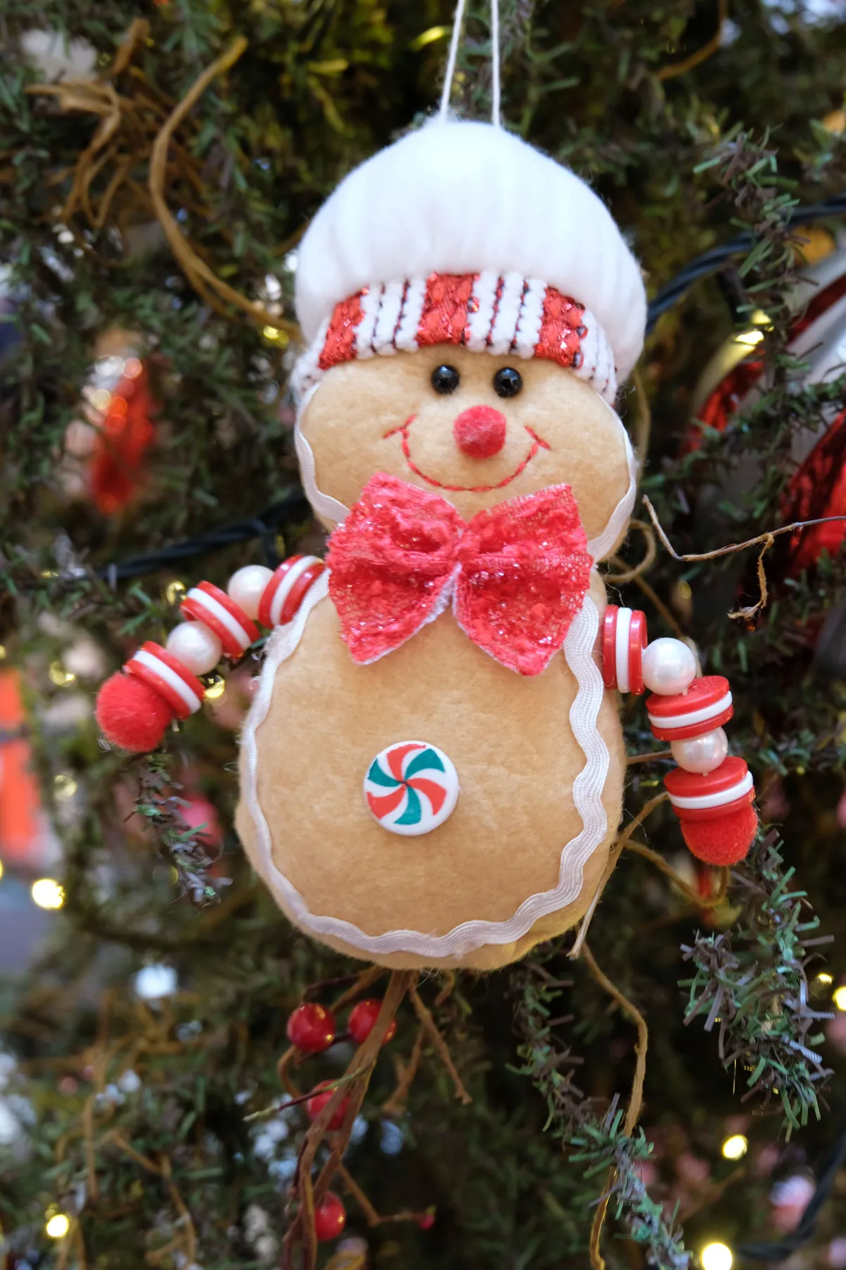 Amusing gingerbread man decoration hanging on a decorated Christmas tree with festive lights.