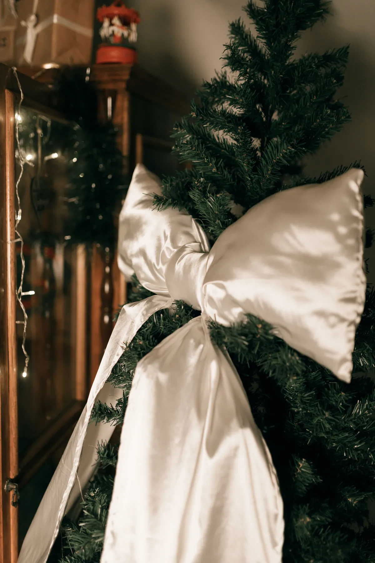 An elegantly decorated Christmas tree with a large white satin bow, indoors.