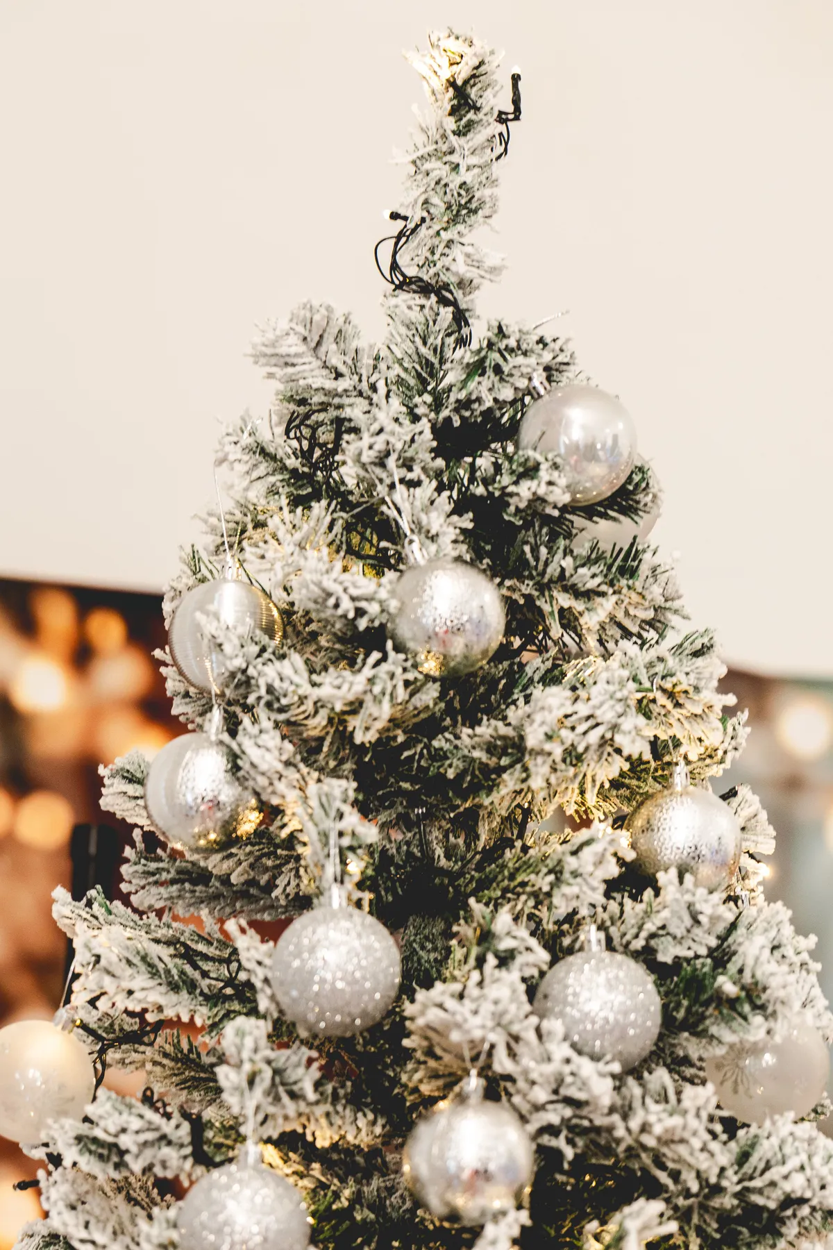 Beautifully decorated Christmas tree with snow effect and silver ornaments indoors.