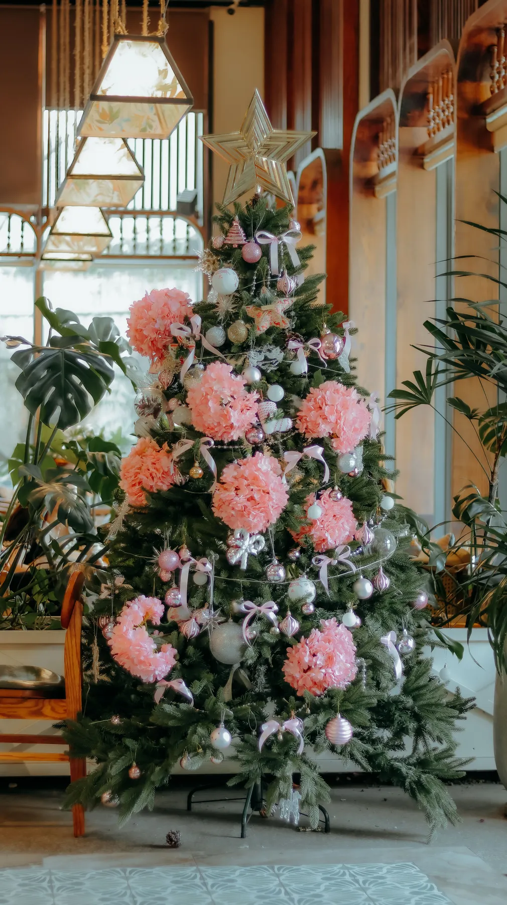 Beautifully decorated Christmas tree with pink florals and star topper indoors.