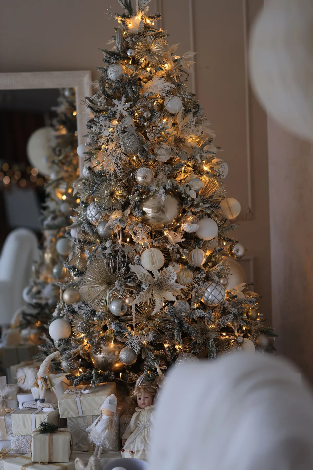 Beautifully decorated Christmas tree with silver and white ornaments, softly lit indoors for a festive ambiance.