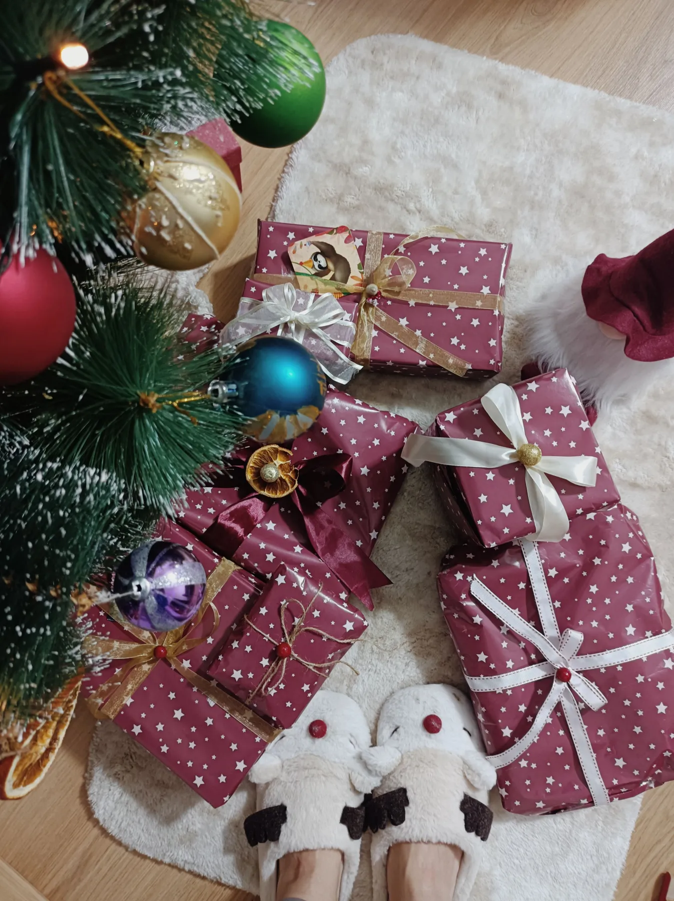 Christmas presents under a tree with ornaments and festive slippers creating a cozy holiday atmosphere.