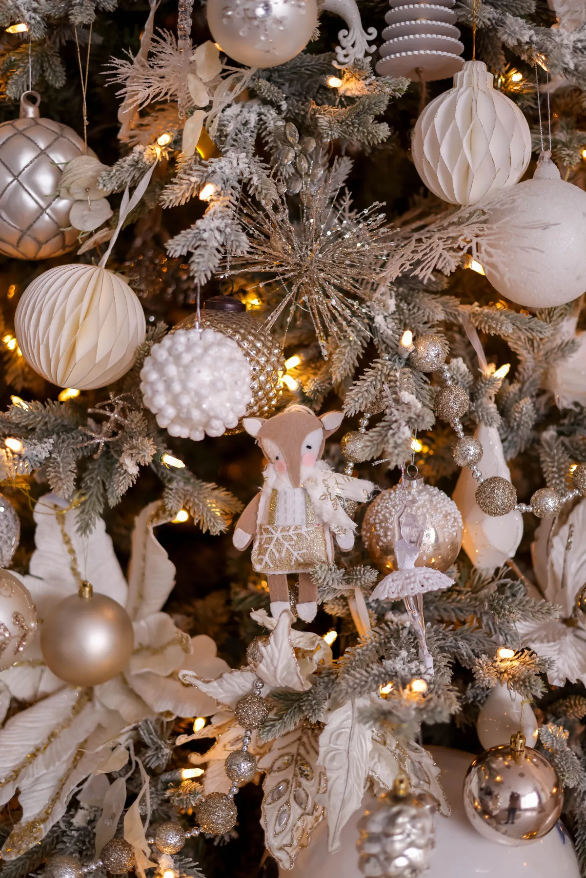 Close-up of a beautifully decorated Christmas tree with gold and white ornaments, sparkling lights, and intricate details.