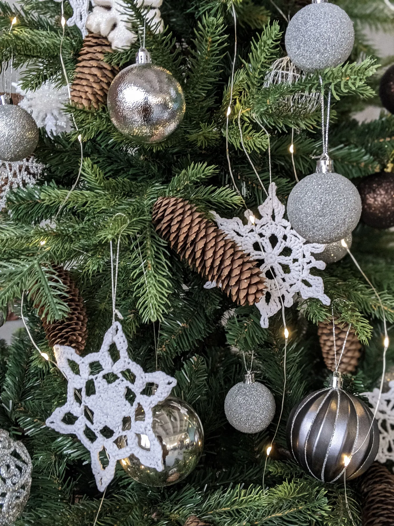 Close-up of a Christmas tree decorated with ornaments, snowflakes, and pinecones, creating a festive and cozy holiday atmosphere.