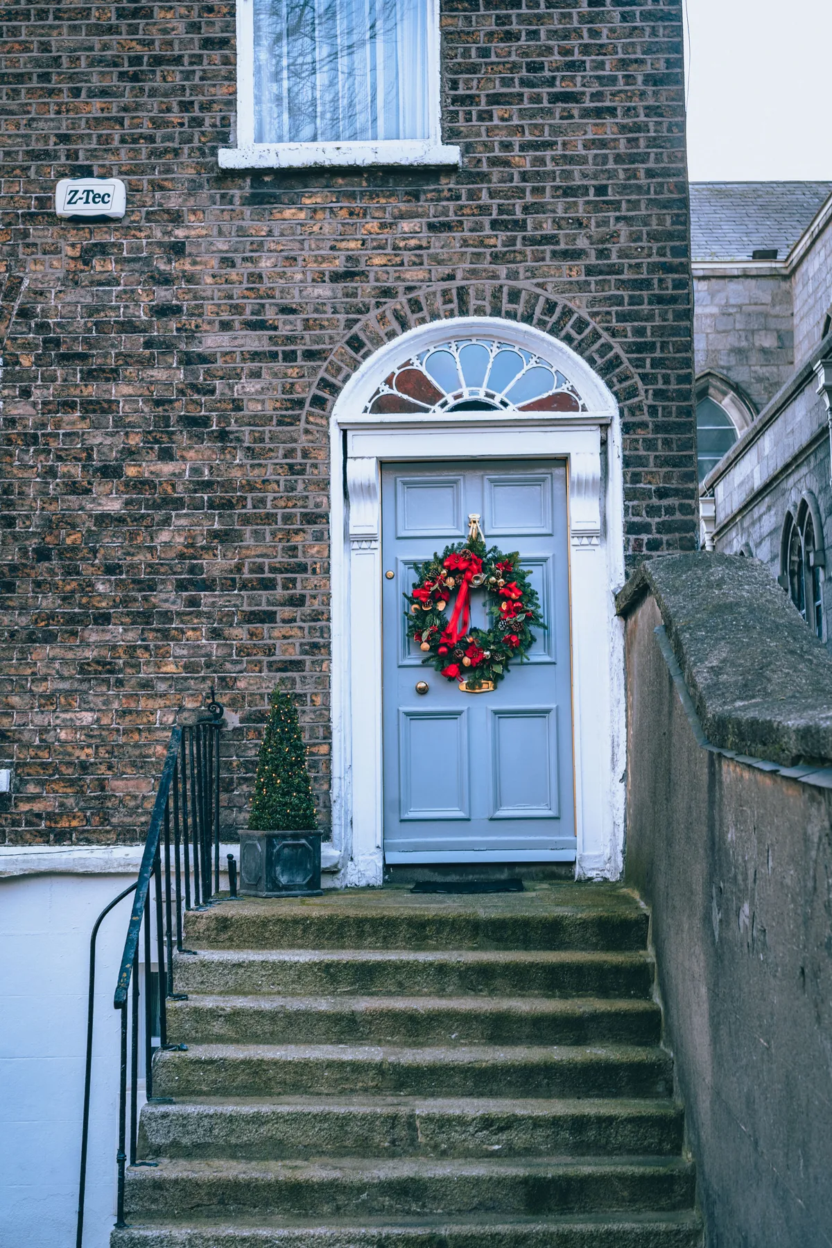 Decorative wreath adorns a blue door of a historic brick townhouse, creating a warm holiday atmosphere.