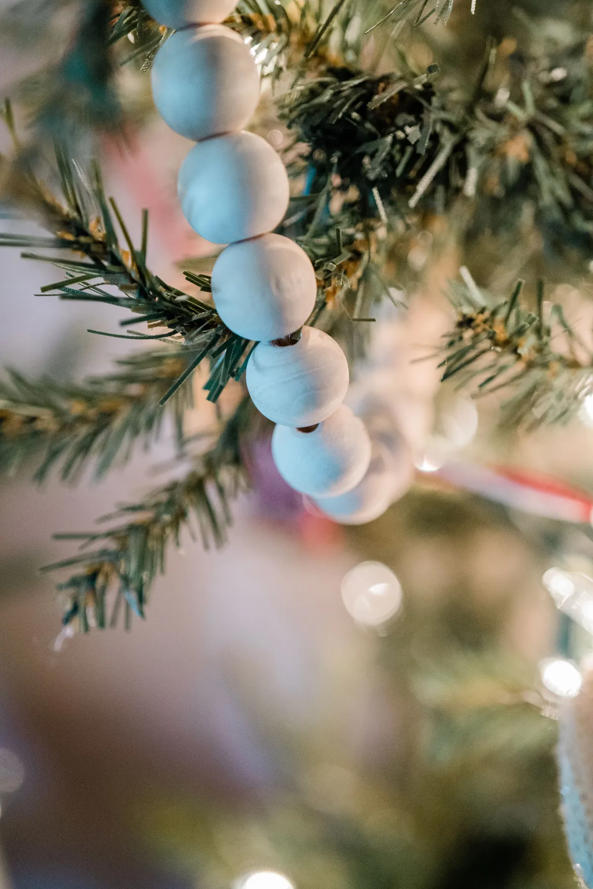Detailed view of a Christmas tree branch with a wooden bead garland and lights.