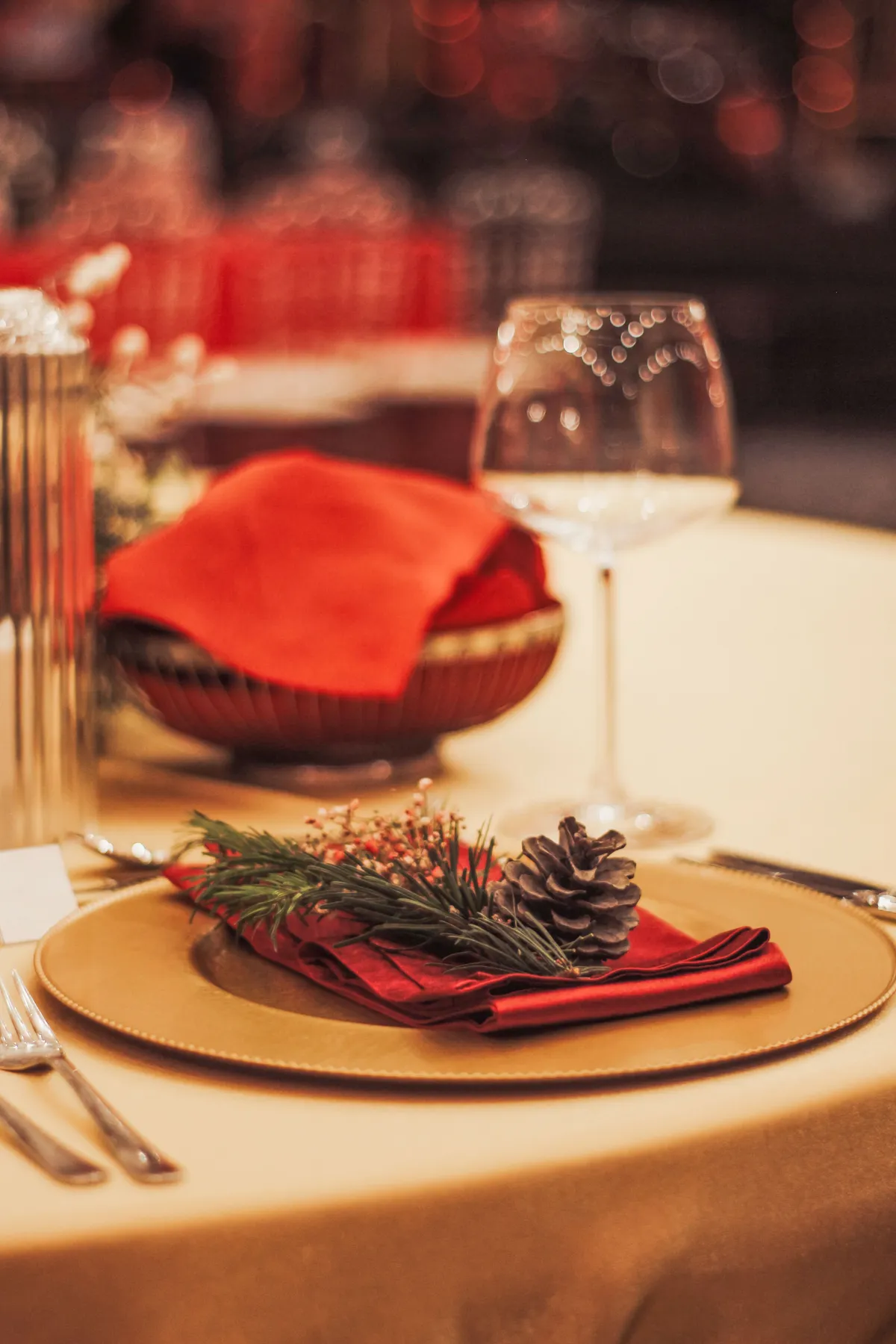 Elegant holiday dining table setup with red accents, pinecone decor, and wine glasses.