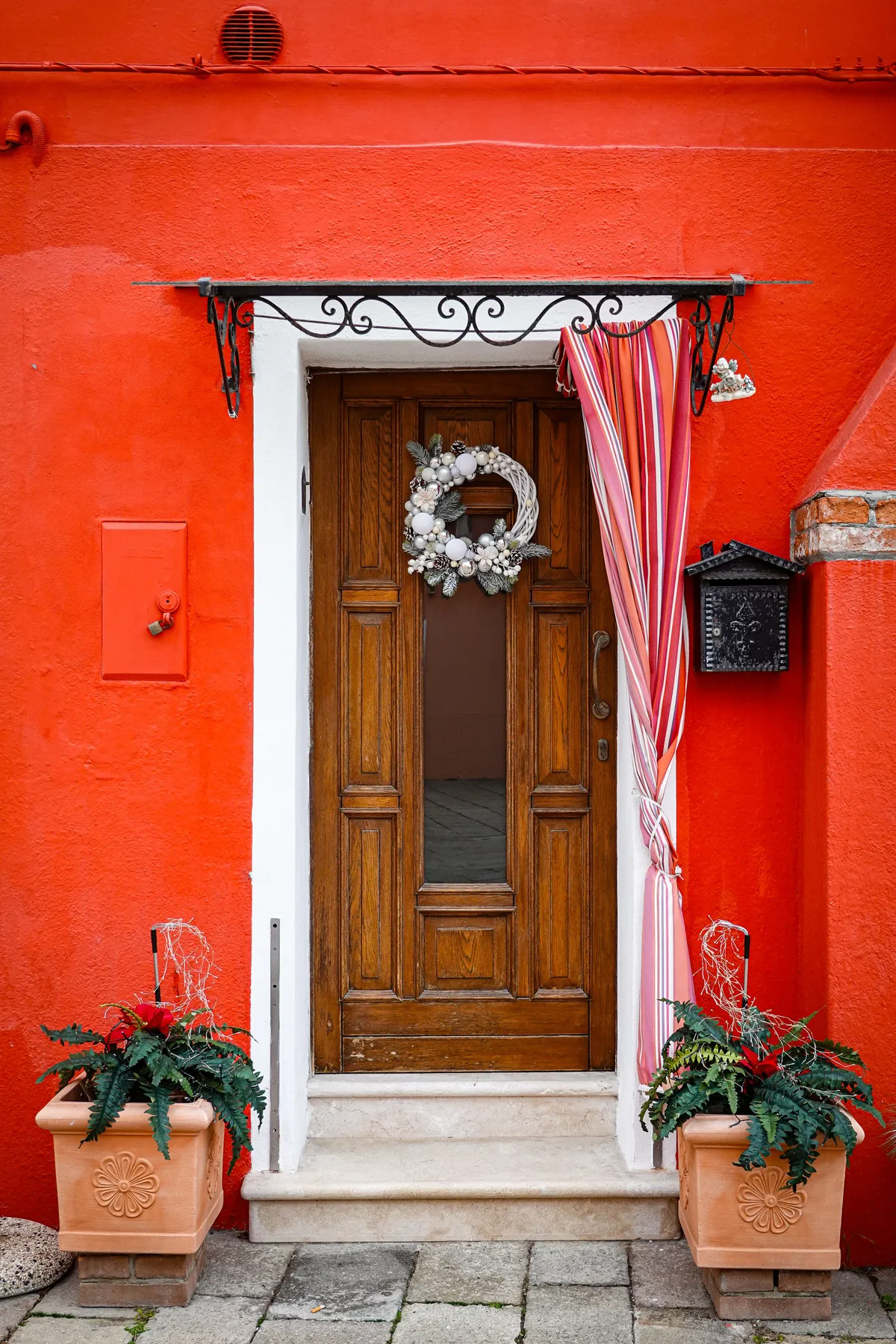 Elegant wooden door with wreath on vibrant red facade, showcasing classic architectural charm.