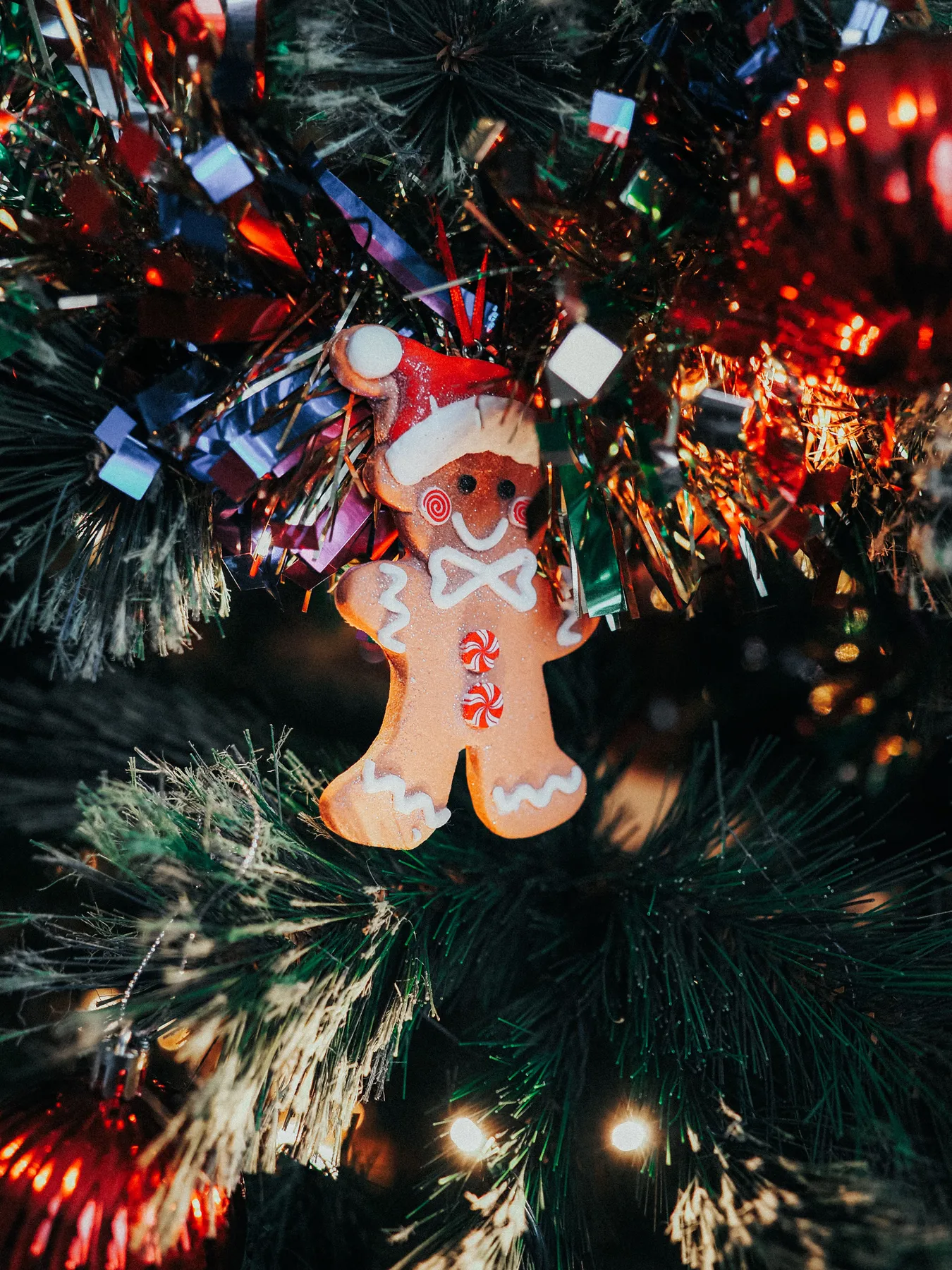 Festive gingerbread man ornament on a decorated Christmas tree branch.