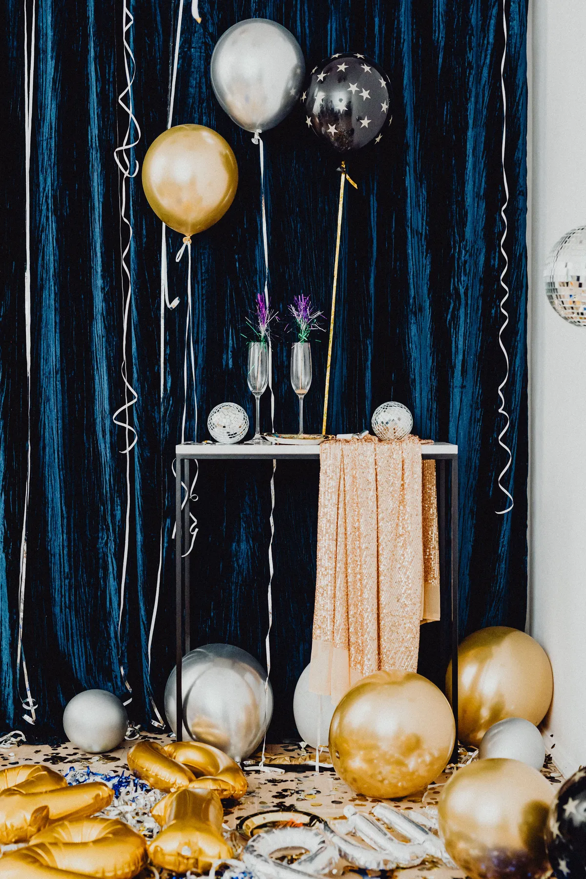 Festive New Year celebration with gold and silver balloons, sparkly tablecloth, and champagne flutes.
