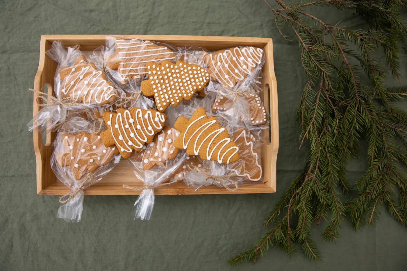 Gingerbread cookies shaped like Christmas trees in a wooden tray with fir branches.