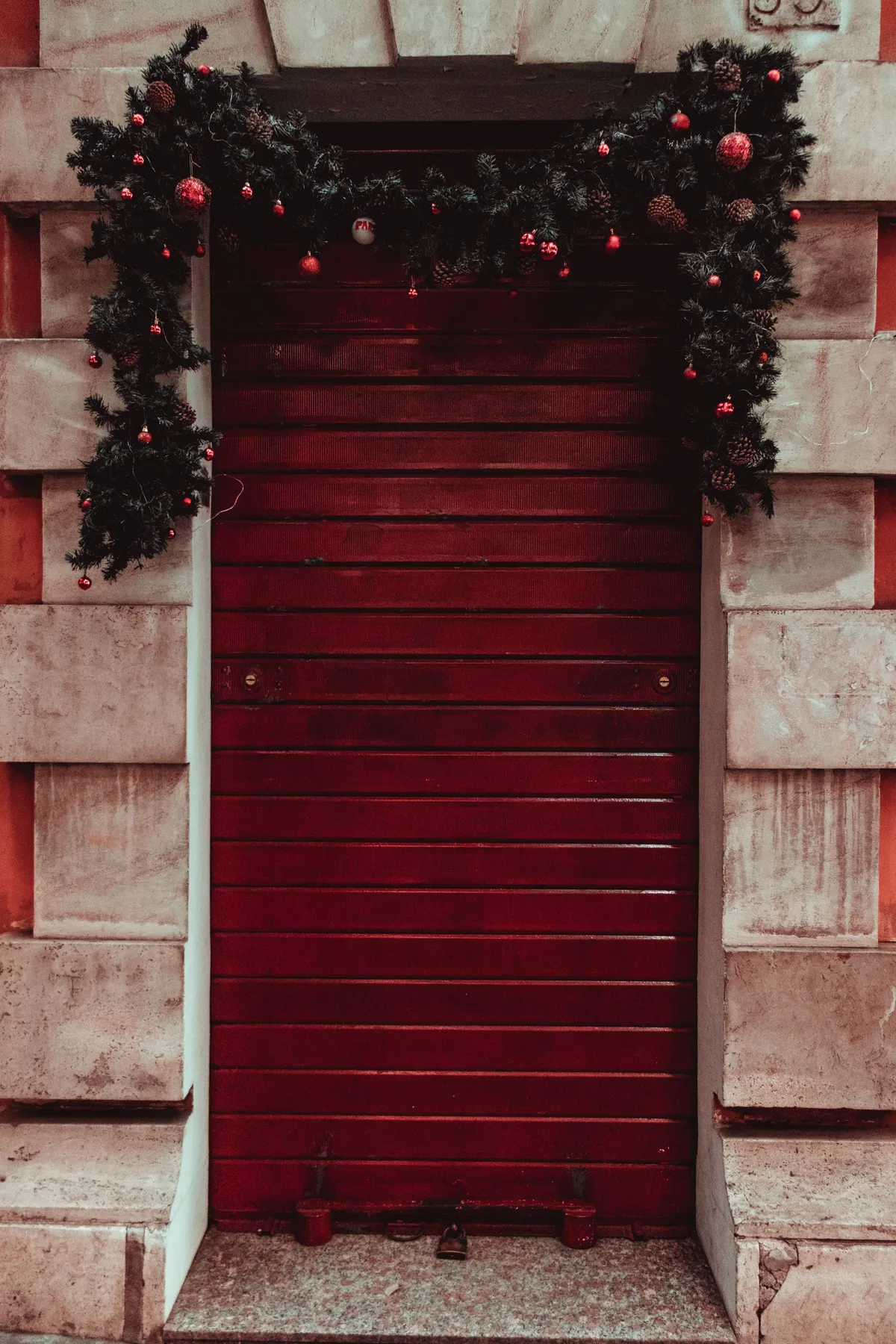 Red wooden door adorned with Christmas garland and ornaments, creating a festive and welcoming entrance.