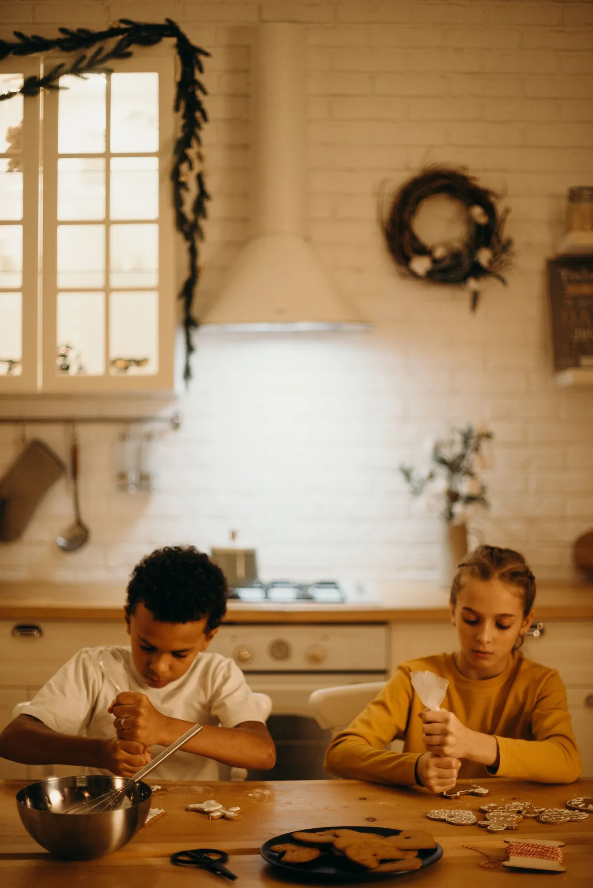 Two children decorate gingerbread cookies in a cozy kitchen setting during the holiday season.