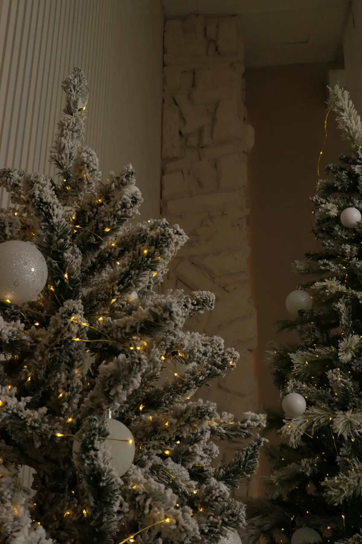 Two frosted christmas trees with lights and ornaments