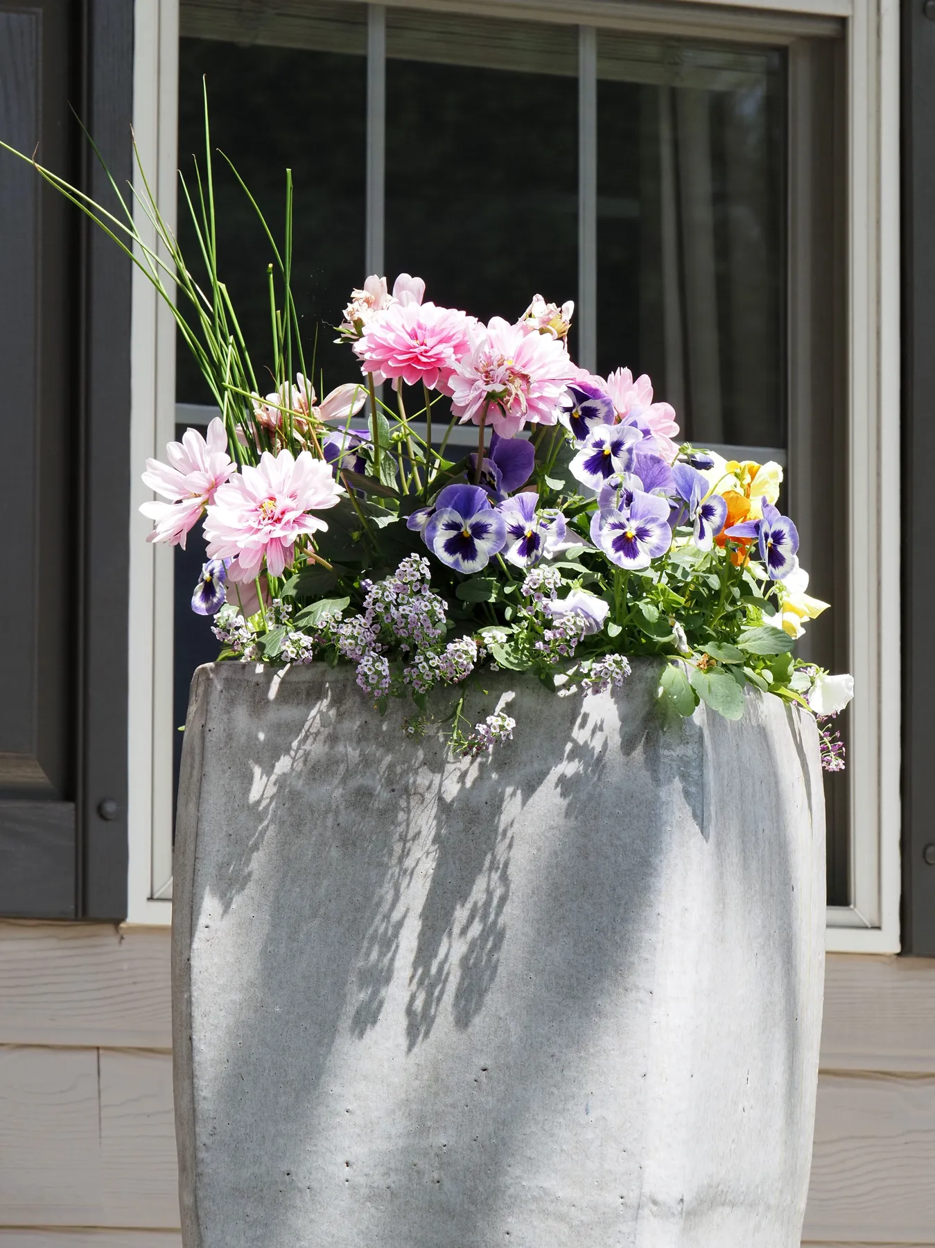 Vibrant pink and purple flowers in a large stone planter outside a window, Doylestown, PA.