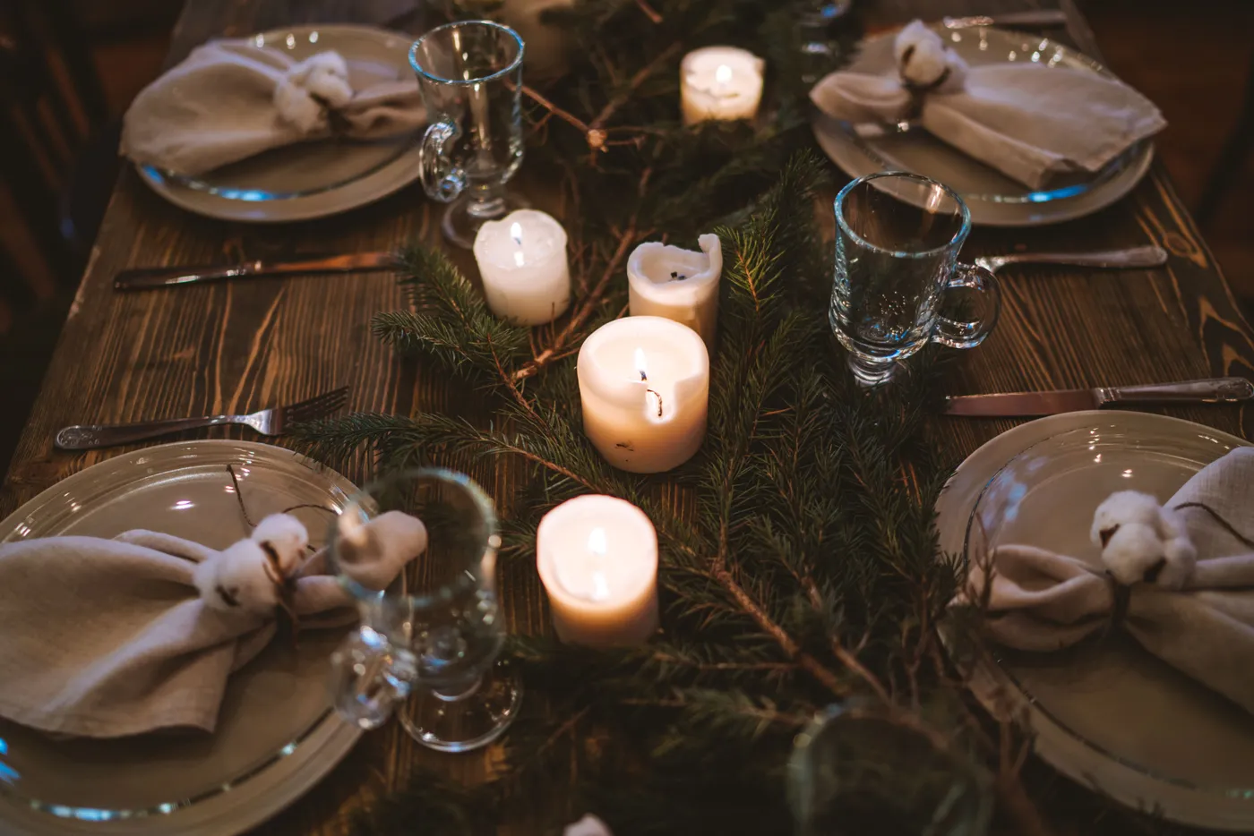 Warm and elegant Christmas table with candles, glassware, and pine decor for festive dining.