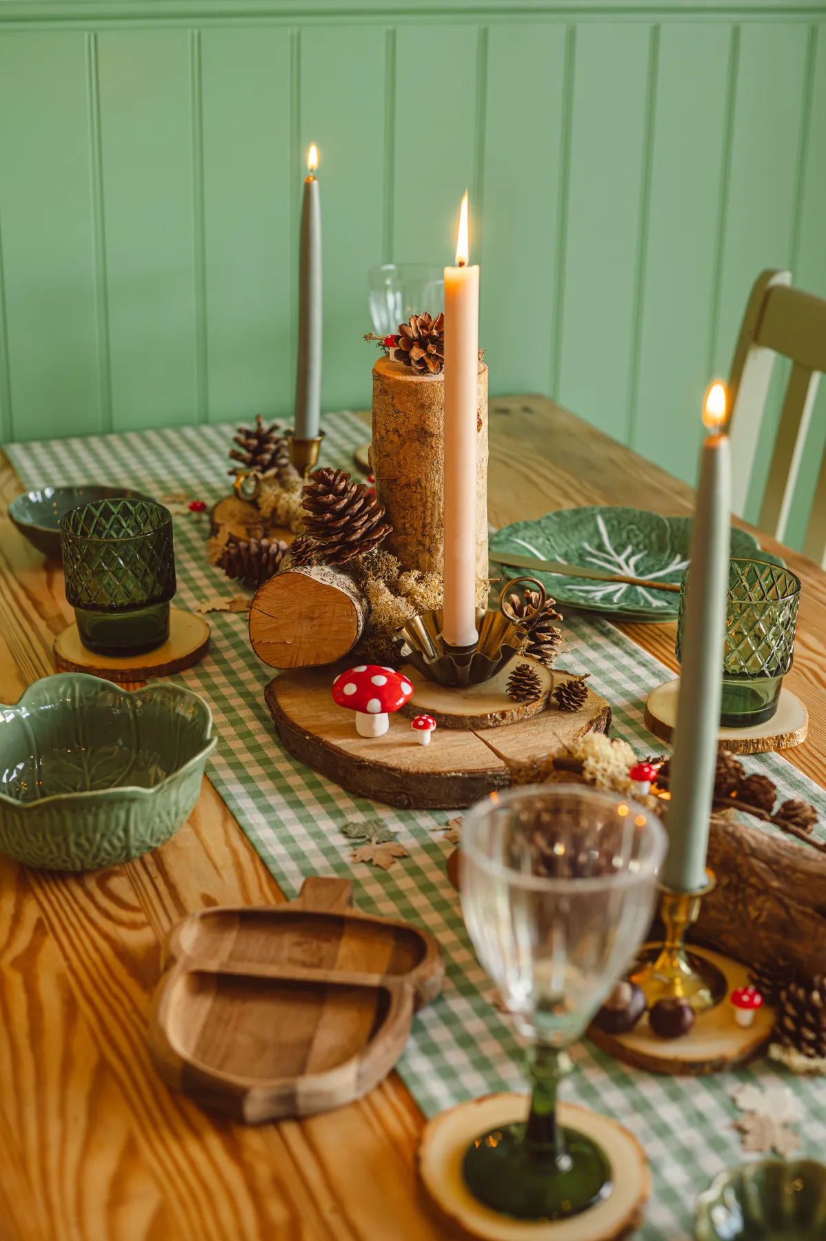 Warm fall table setting with candles and pinecones on a wooden table.