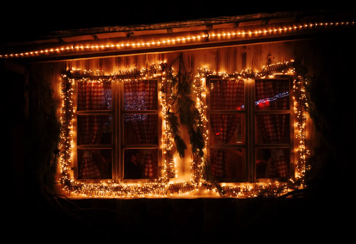 Warm glow of holiday lights framing a window with checkered curtains, creating a cozy winter ambiance.