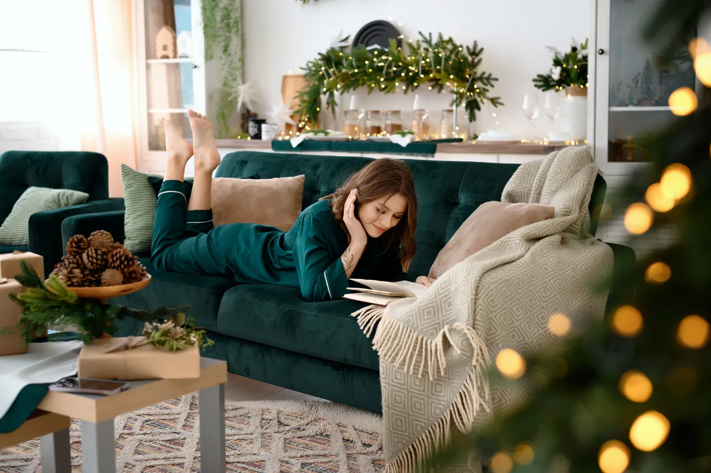 Woman relaxing and reading on a sofa in a Christmas-themed living room with festive decor.