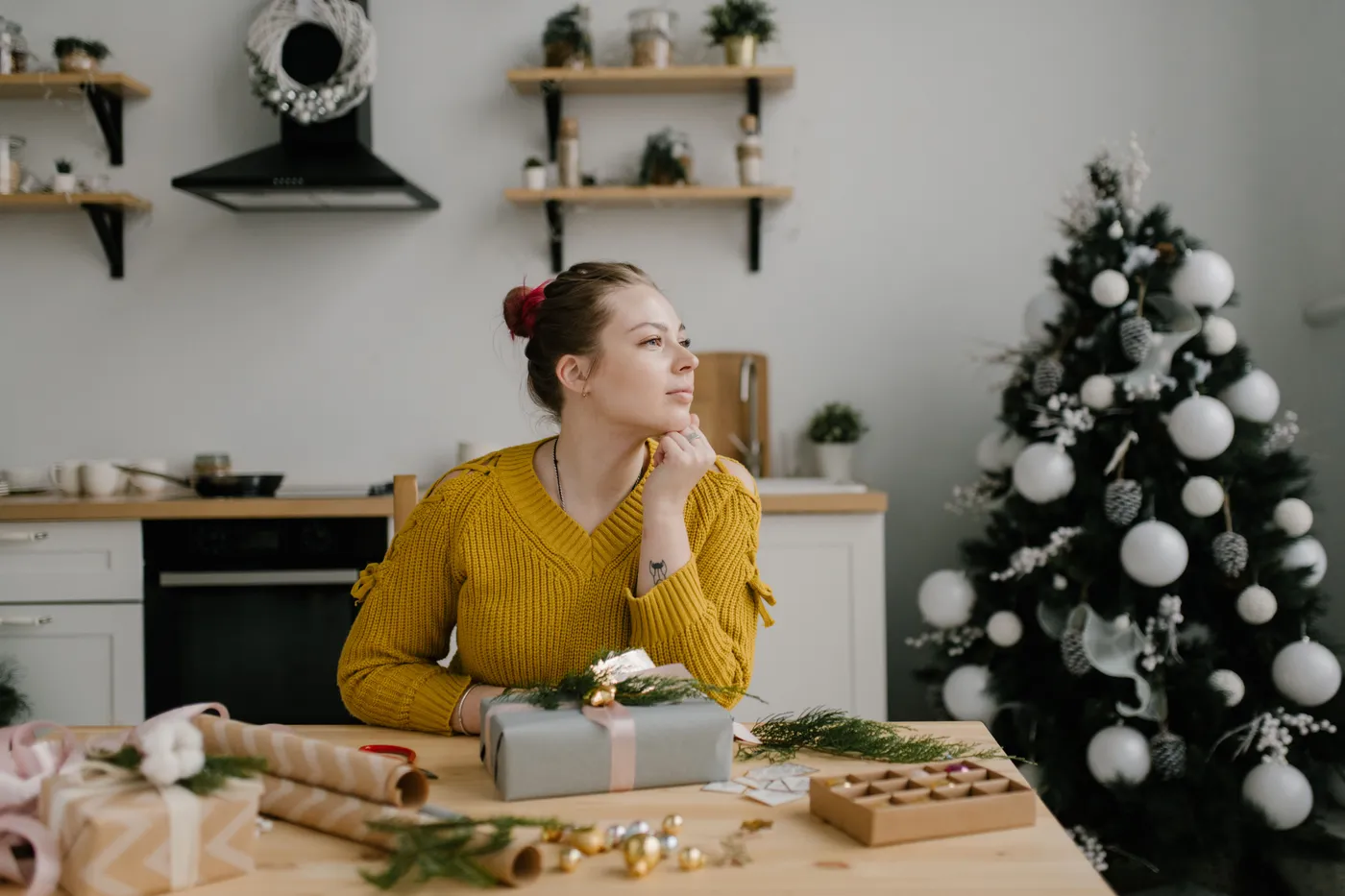 Young woman in cozy sweater daydreams in a festive, decorated kitchen during Christmas.